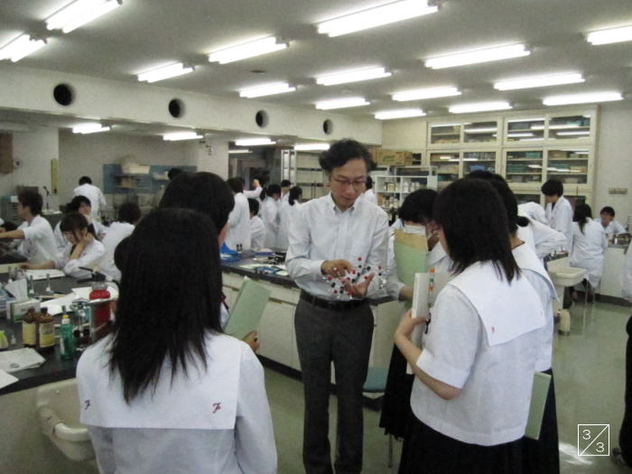 学校見学中の郡山第一中学校の生徒たちが、教員から実験について説明を受けている様子。