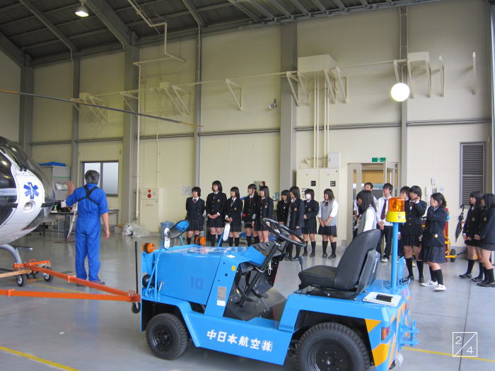福島県立光南高等学校の1年生がヘリコプターの見学をしている様子。青い牽引車の前で、教員が説明を行っている。