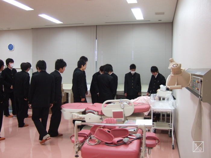 福島県立磐城高等学校の3年生が医療機器を見学している教室の様子。ピンクのベッドや医療器具が配置されている。