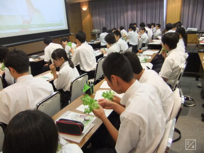 学校見学中の会津学鳳中学校の3年生が、講義を受けながら緑の葉を手にしている様子。