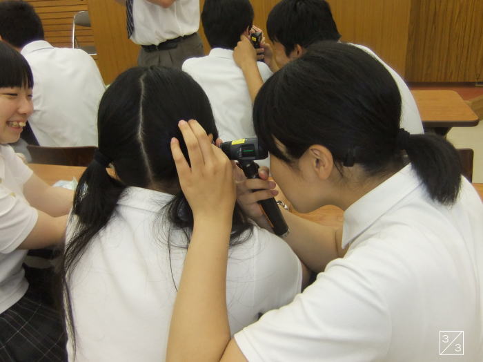 中学生が学校見学中に、友人の耳を観察する様子。楽しそうな雰囲気が伝わる。