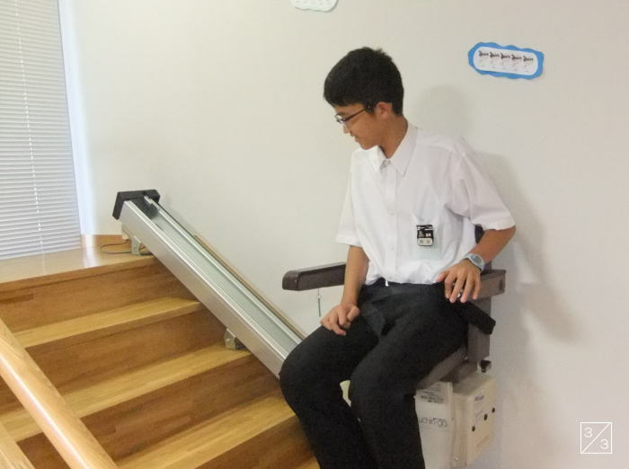 学校の階段に設置された昇降機に座る中学生の男の子。