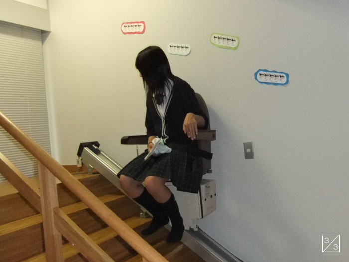 階段に設置された昇降機に座る女子学生の姿。学校見学の一環で撮影された。