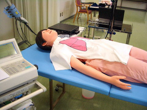 フィジカルアセスメントモデル「フィジコ」が青いテーブルの上に横たわっている様子。医療教育用の人形で、胸部には解剖図が描かれている。