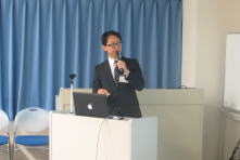心エコーセミナーで講演を行う男性が、パソコンを前にして話している様子。背景には青いカーテンが掛かっている。