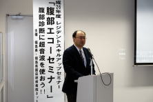 平成26年度腹部エコーセミナーで講演する男性が、壇上で話している様子。背景にはセミナーの案内が掲示されている。