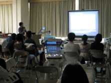心エコーセミナーのセッション中、講師がスクリーンを使って説明している様子。参加者が椅子に座り、真剣に聴講している。