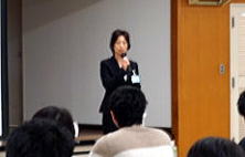心エコーセミナーで講演を行う女性がマイクを持ち、聴衆に向かって話している様子。