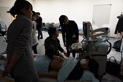 腹部エコーセミナーでの実習風景。受講者が患者にエコー検査を行い、指導者がサポートしている様子。