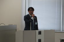 腹部エコーセミナーで講演を行う男性がマイクを持って話している様子。
