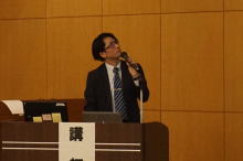 腹部エコーセミナーで講演を行う男性が、資料を指し示しながら説明している様子。
