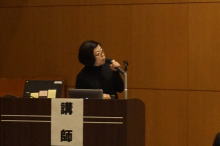 腹部エコーセミナーで講演を行う女性講師がマイクを持って話している様子。
