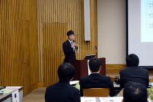 研修医の武藤雄紀先生が福島県地域医療症例検討会で発表している様子。背景には木製の壁とプロジェクターが映し出されています。