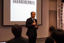 福島県地域医療症例検討会で講演する男性の姿。背景にはタイトルが表示されている。