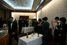 医療関係者が集まる会場で、食事や飲み物を楽しむ様子。スーツ姿の参加者が多く、交流が行われている。
