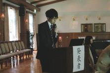福島県地域医療症例検討会で発表する研修医の菊田春彦先生。壇上でマイクを持ち、聴衆に向けて話している様子。