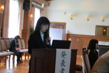 研修医の佐久間真悠先生が発表を行っている様子。背景には聴衆が座っている。