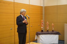 福島県立医科大学で行われた地域医療症例検討会の様子。スーツを着た男性がマイクの前で話している。テーブルには3つの彫刻が置かれている。