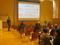 心電図セミナーで講演を行う講師と、聴講する参加者たちが映る会場の様子。