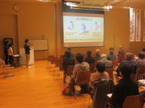 心電図セミナーで講演を行う講師と参加者が座っている様子。スクリーンには心電図に関する情報が表示されている。