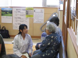 医療従事者が高齢者と対話している様子、背景にはカレンダーやポスターが見える。