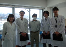 医療体験プログラムに参加する学生たちが白衣を着て並んでいる様子。背景には窓からの景色が見える。