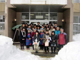 医療・福祉体験プログラムに参加した学生たちが雪に囲まれた建物の前で集合写真を撮影している様子。