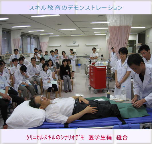医学生によるスキル教育のデモンストレーションの様子。患者役の男性と周囲の医学生たちが真剣に学んでいる。