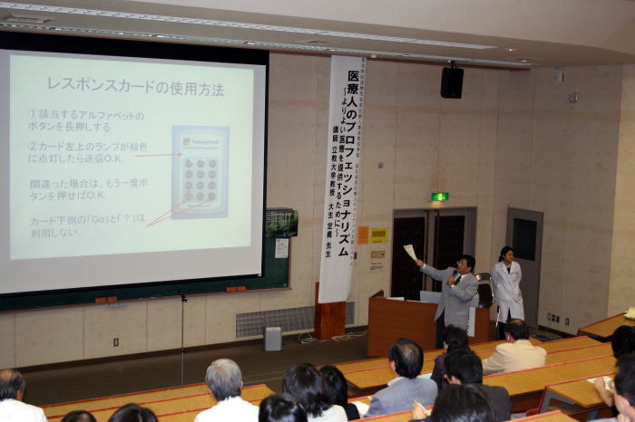 医療人のプロフェッショナリズムに関する講演会の様子。講師がレスポンスカードの使用方法を説明している。