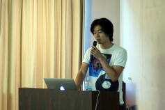 福島県立医科大学の講演者がマイクを持ち、プレゼンテーションを行っている様子。