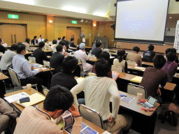 第2回福島アドバンスド・コースの参加者が講演を聴いている様子。会場には多くの人が集まり、スクリーンにはプレゼンテーションが映し出されている。
