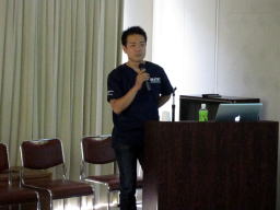福島県立医科大学の講義で話す講師、背景には椅子とパソコンがある。