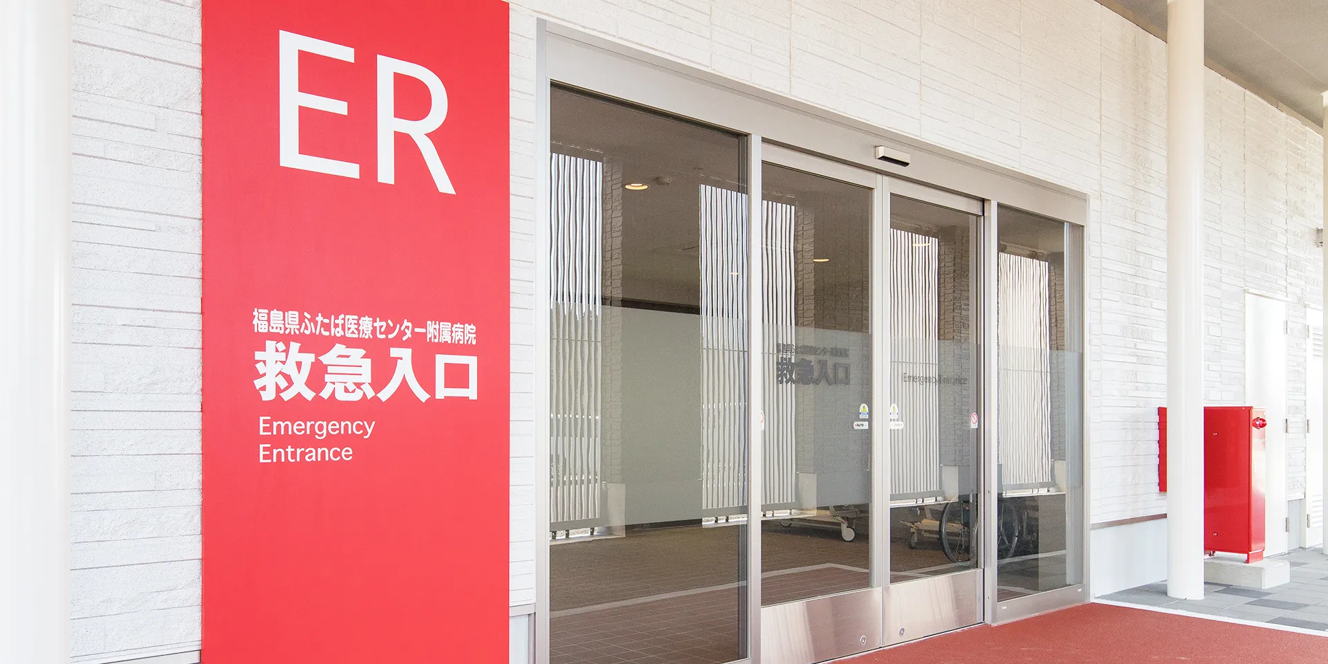 福島県ふたば医療センターの救急入口を示す赤い看板とガラス扉の画像。