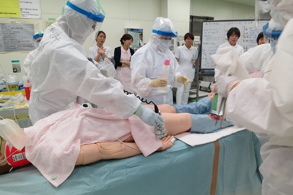 医療研修会での模擬患者に対する緊急被ばく医療の実習風景。参加者が防護服を着用し、手順を学んでいる。