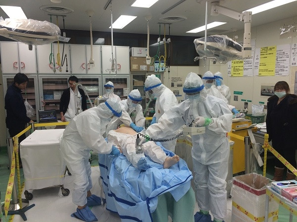 院内緊急被ばく医療研修会の様子。防護服を着た医療スタッフが模擬患者に対応している。