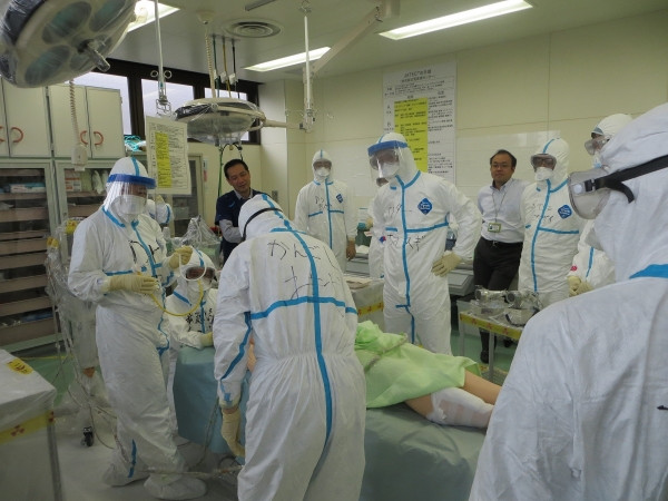 福島災害医療セミナーでの医療従事者が患者を治療している様子。防護服を着た医師たちが集まり、真剣な表情で対応している。