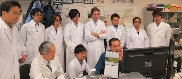 早稲田大学の梅津教授と大学院生たちが、コンピュータの前で研究について話し合っている様子。