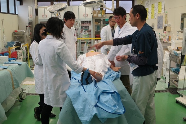 医学生たちが放射線測定実習で防護服を着用し、模擬患者の初期診療を行っている様子。
