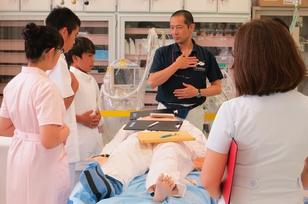 中学生が職場体験で医療現場を見学し、指導者から説明を受けている様子。