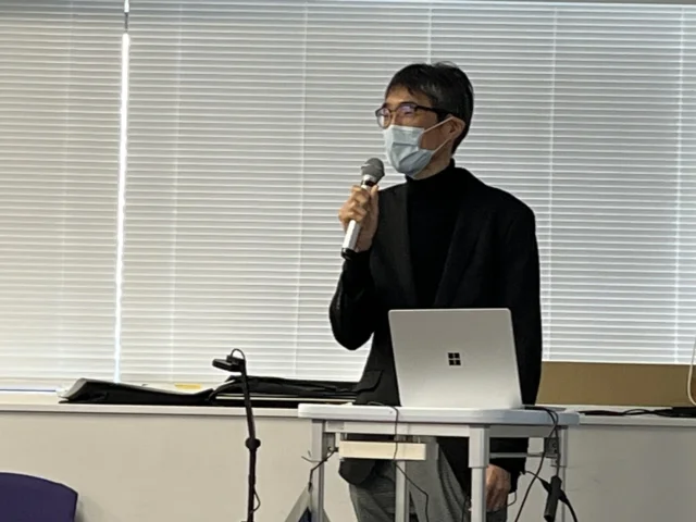 看護師特定行為研修のフォローアップセミナーで講演する男性が、マイクを持って話している様子。