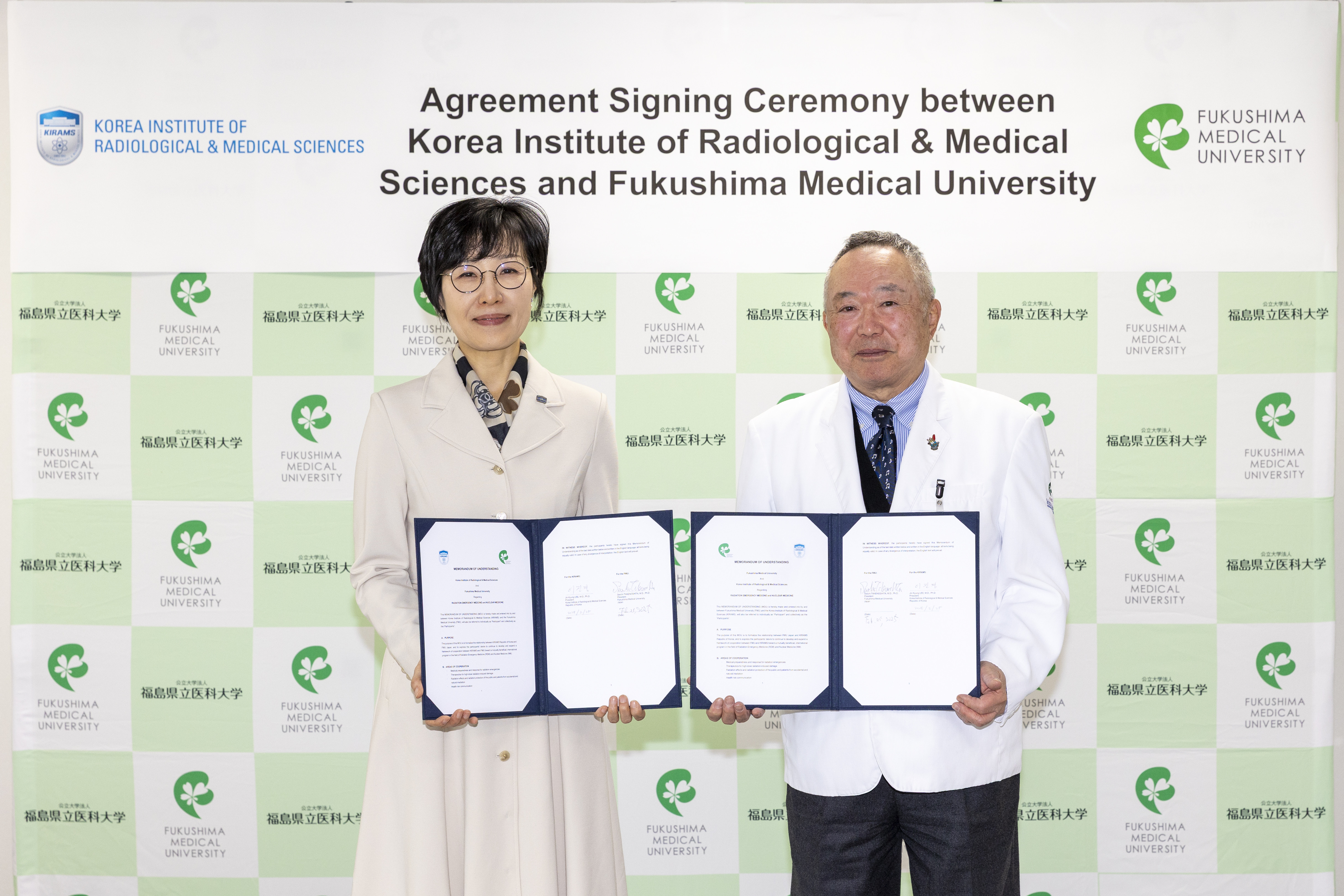 韓国原子力医学院とのMOU締結式で、書類を持つ二人の代表者が笑顔で立っている様子。