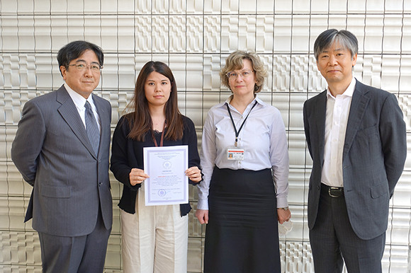 座喜味ありささんが修了証を持ち、北西医科大学の教員と共に記念撮影をしている様子。