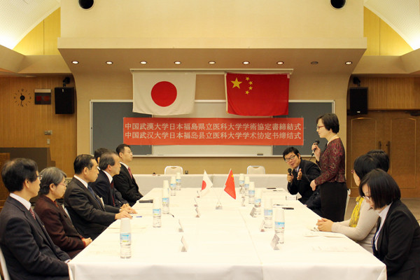 中国武漢大学医学部との学術交流に関する協定締結式の様子。日本と中国の国旗が掲げられ、参加者がテーブルを囲んでいる。