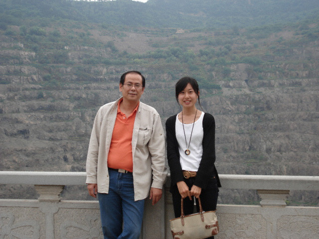 男性と女性が山の背景の前でフェンスに寄りかかって立ち、女性はバッグを持っています。