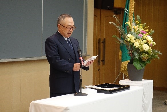 大学院医学研究科の入学式でスピーチをする男性と花が飾られた壇上の様子。