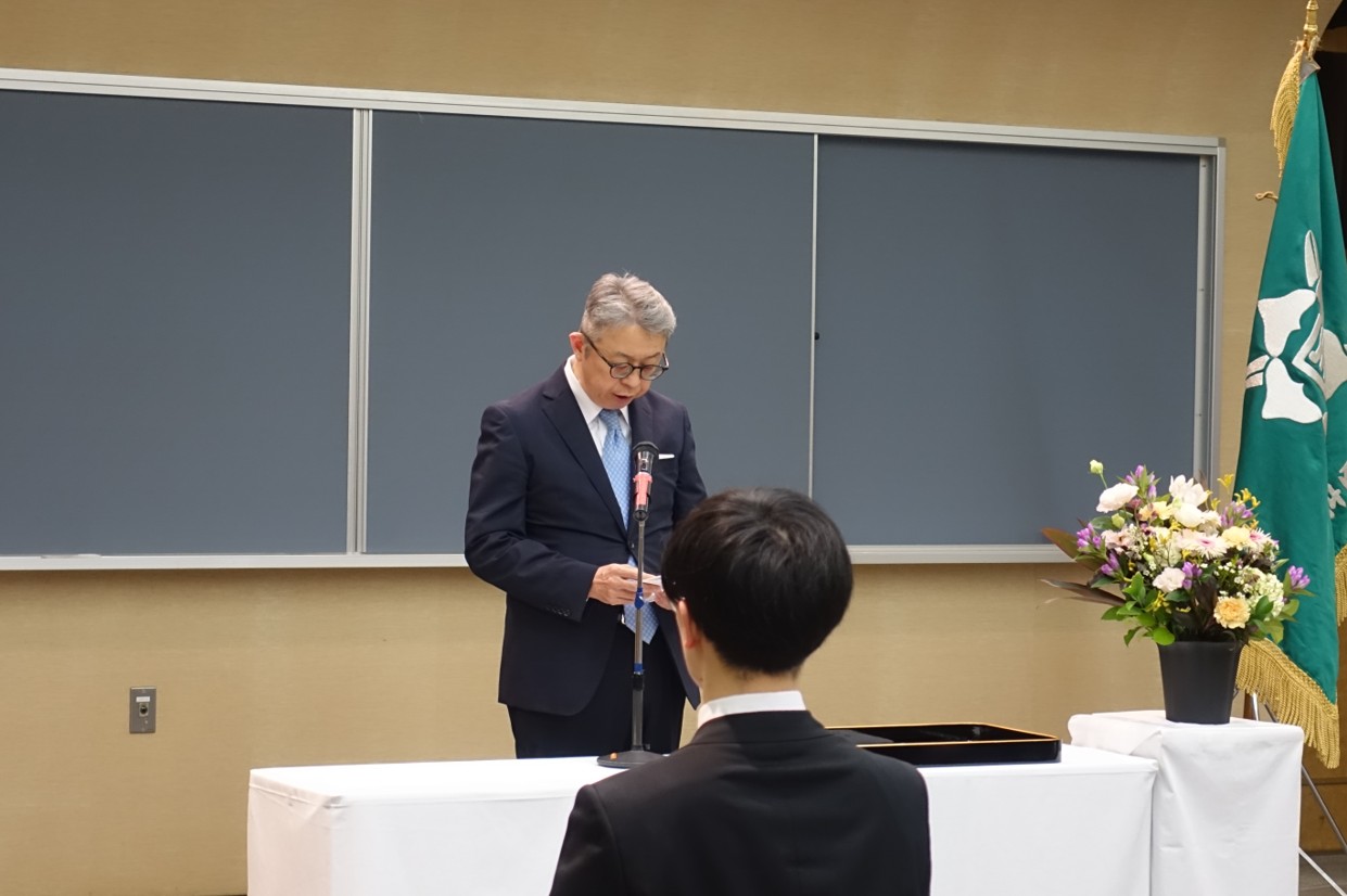 大学院医学研究科の入学式でスピーチをする鈴木学長と花が飾られた壇上の様子。