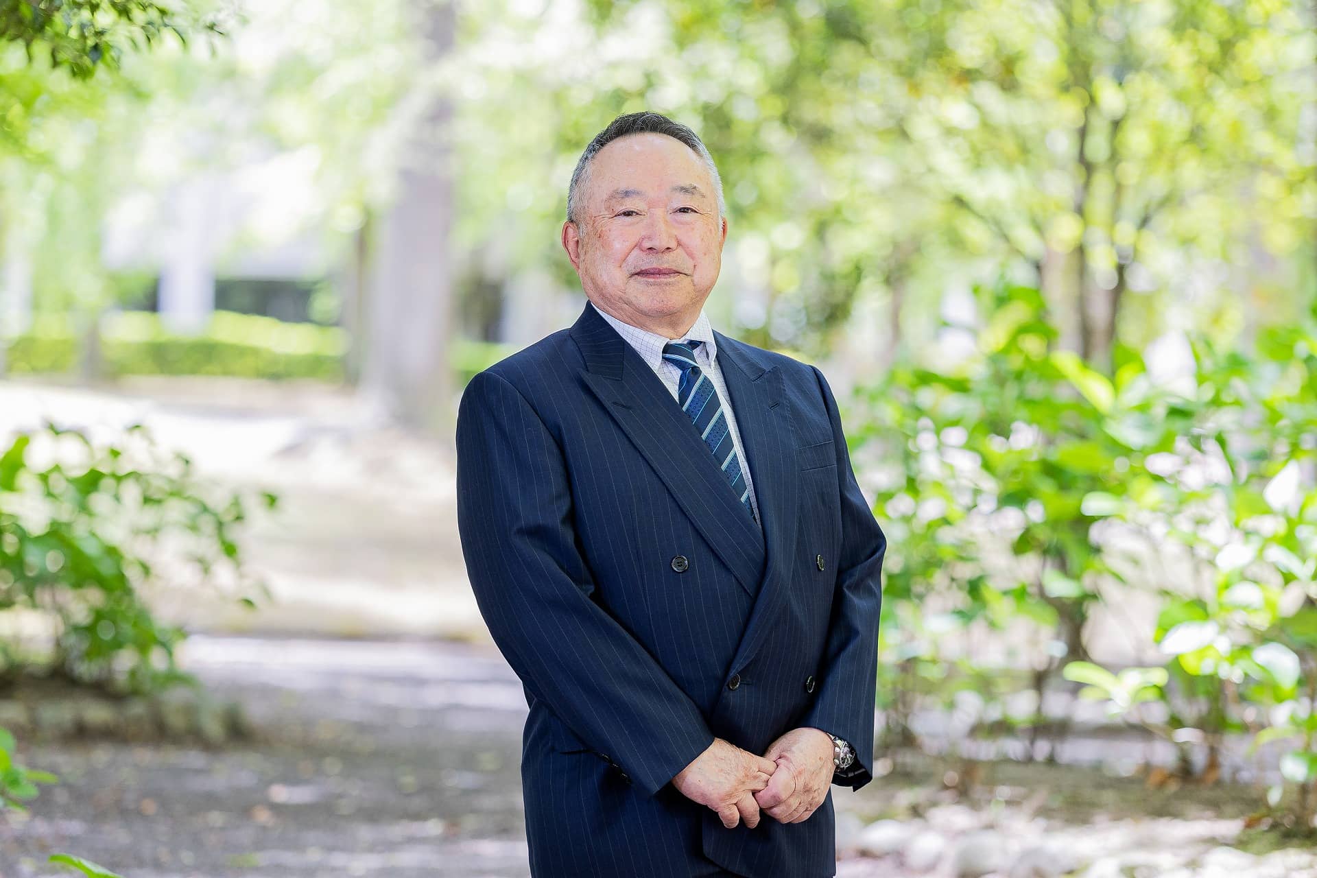 理事長兼学長の竹之下誠一氏が緑豊かな公園で立っている写真。