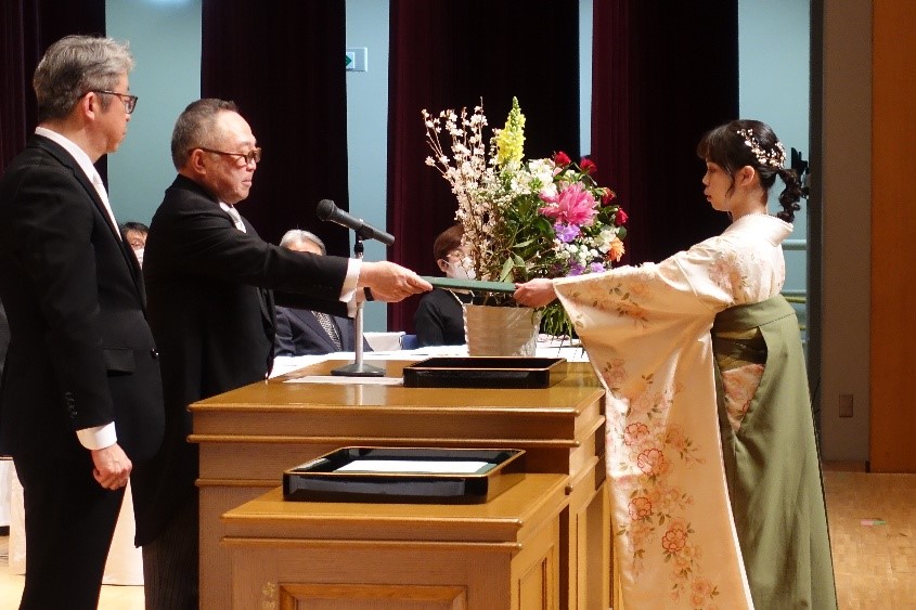 学位記授与式で卒業生が学位記を受け取る様子。華やかな装飾と花が飾られた壇上での感動的な瞬間。