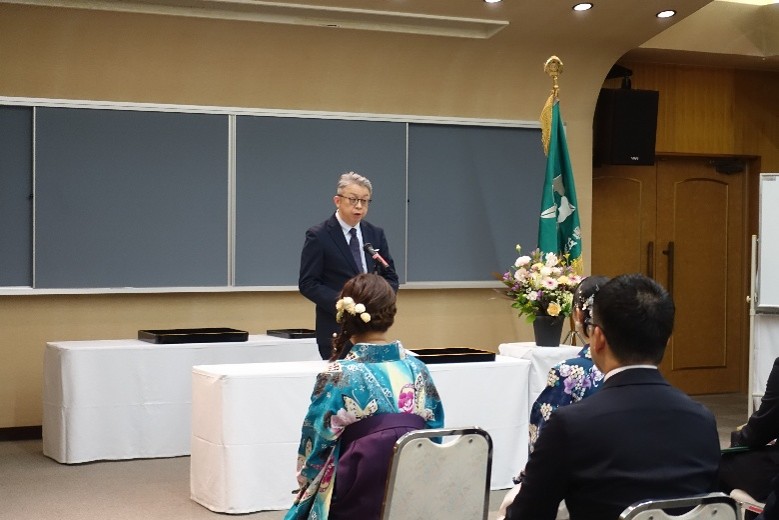 大学院の学位記授与式でスピーチをする鈴木学長と、参加者たちの様子。