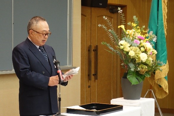 大学院の学位記授与式でスピーチをする男性と華やかな花が飾られたテーブルの様子。